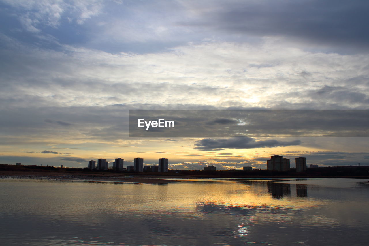 Silhouette buildings by lake against sky during sunset
