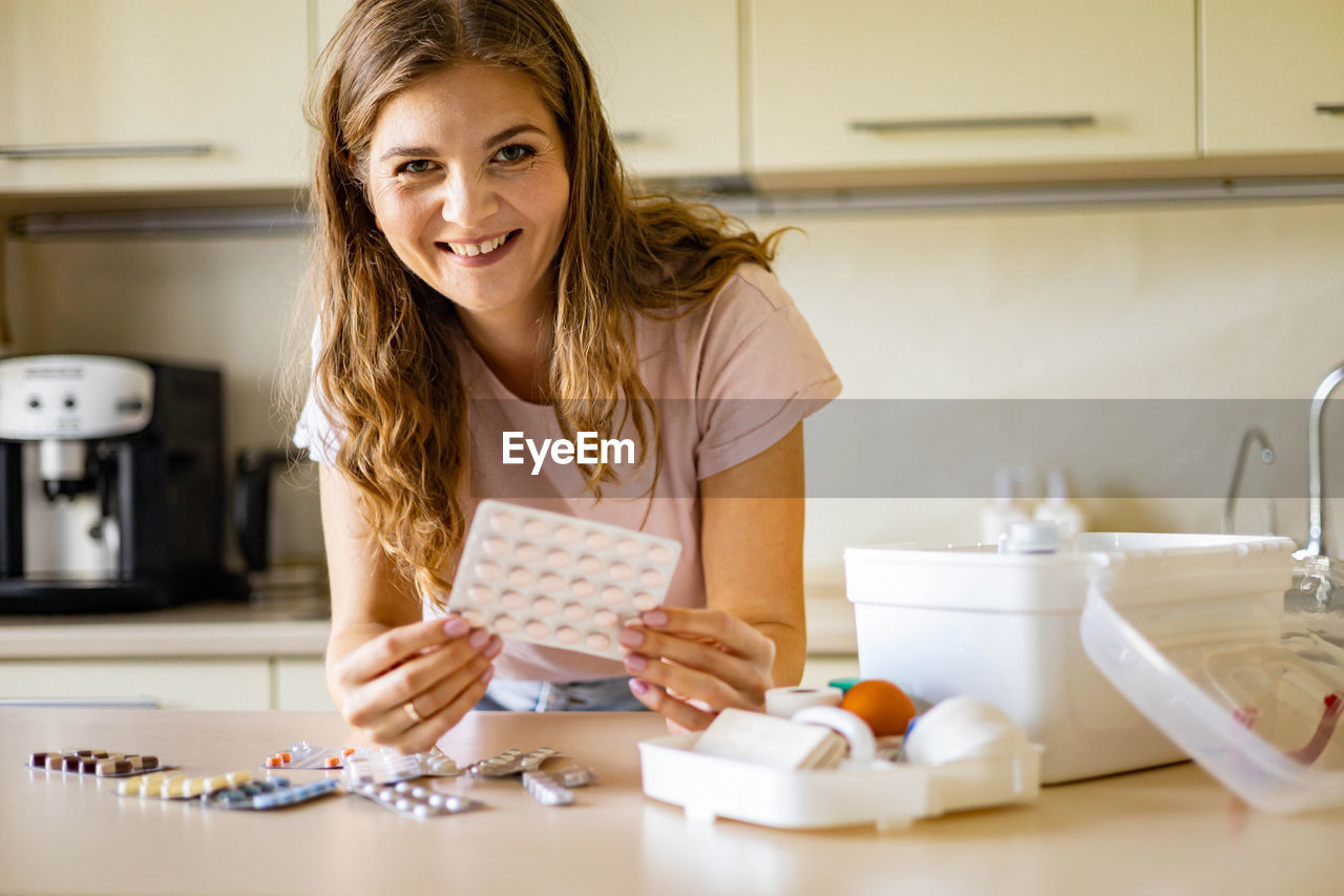 portrait of smiling young woman using mobile phone while sitting in bathroom