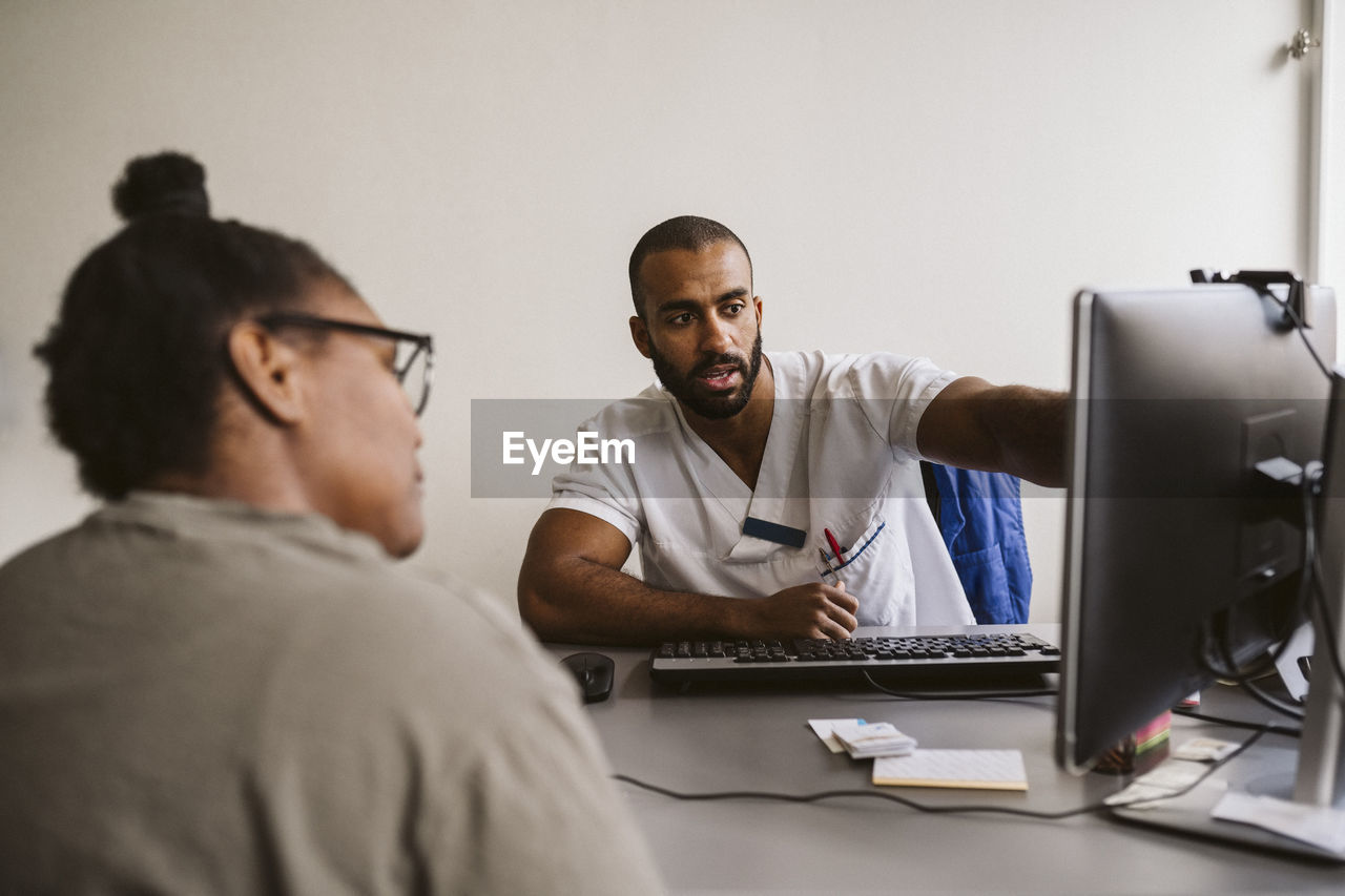 Male healthcare worker discussing over computer with female patient in medical clinic