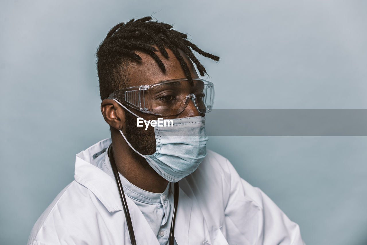 Doctor wearing mask sitting against colored background