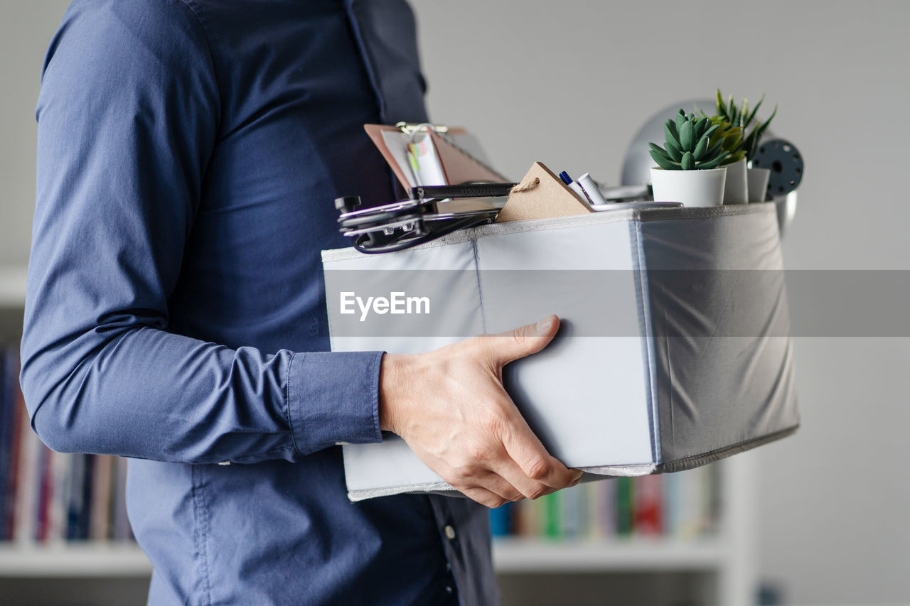 Midsection of man holding cardboard box in office