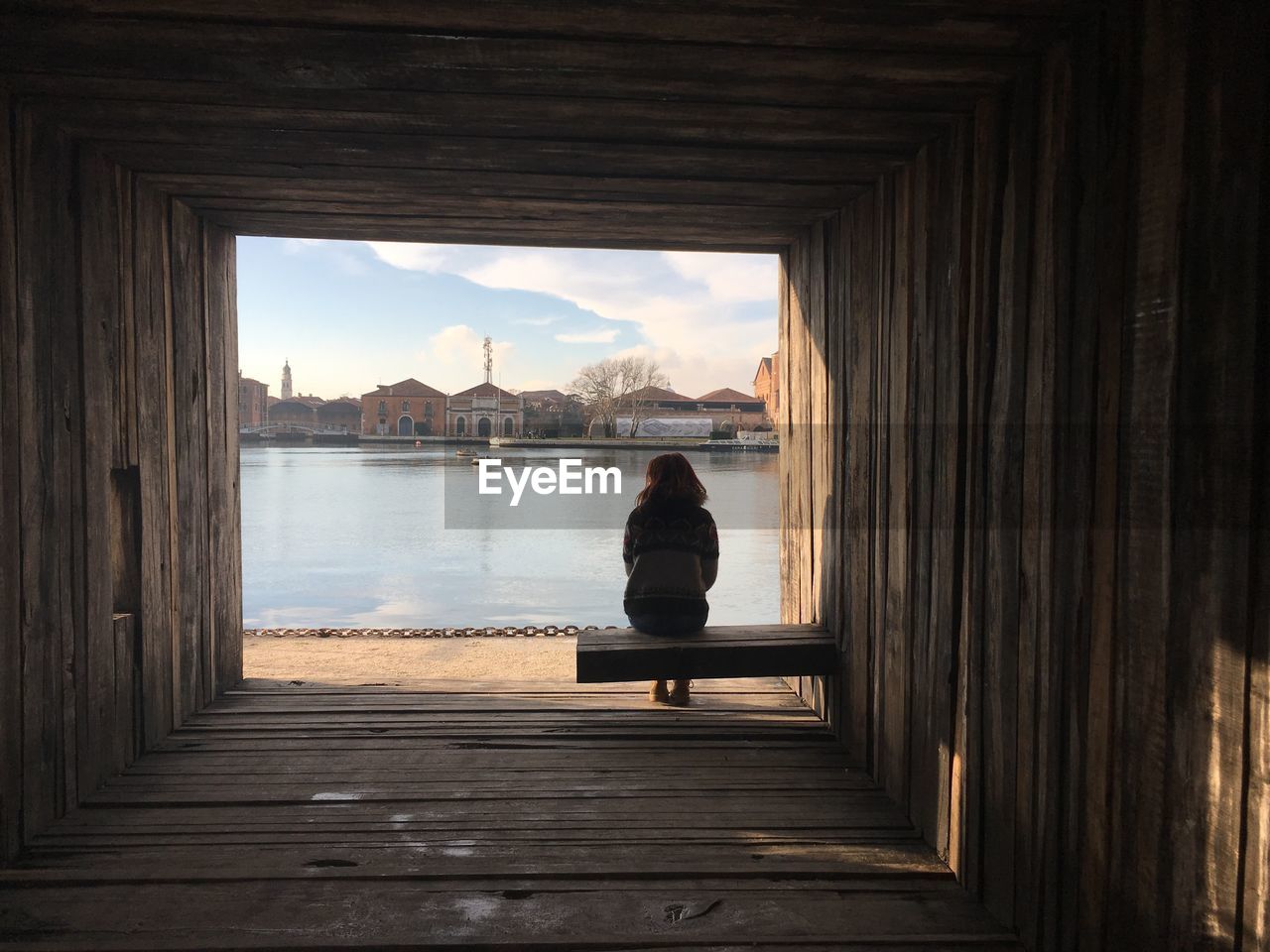 REAR VIEW OF WOMAN SITTING AT SEA SHORE