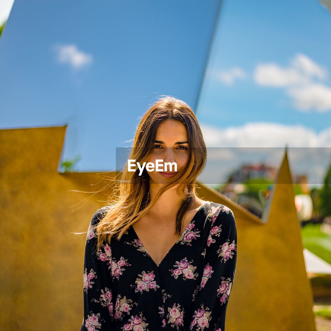 PORTRAIT OF SMILING YOUNG WOMAN STANDING OUTDOORS