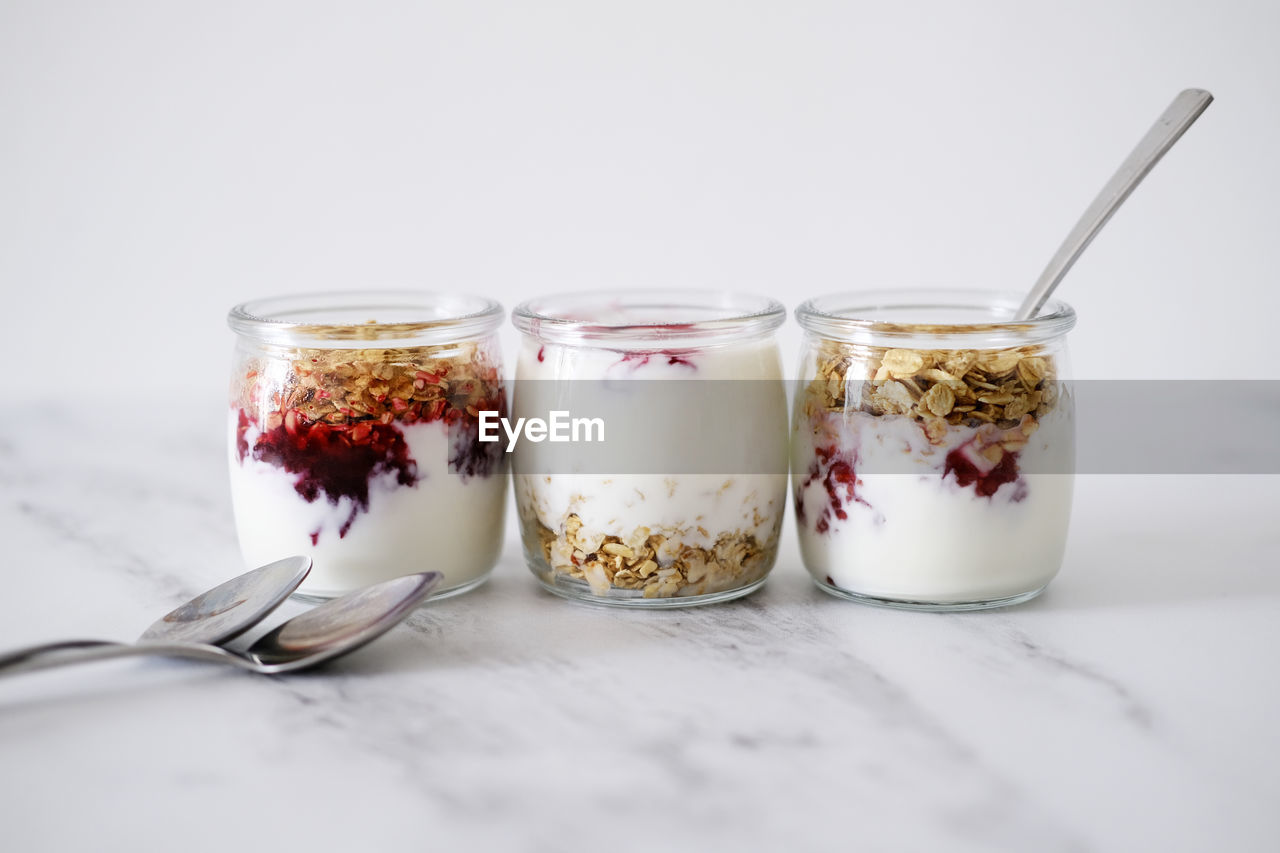 Three jars of oat granola with greek yogurt and nuts on a light background