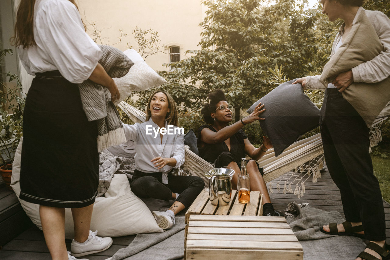 Cheerful females taking cushions from friends during social gathering