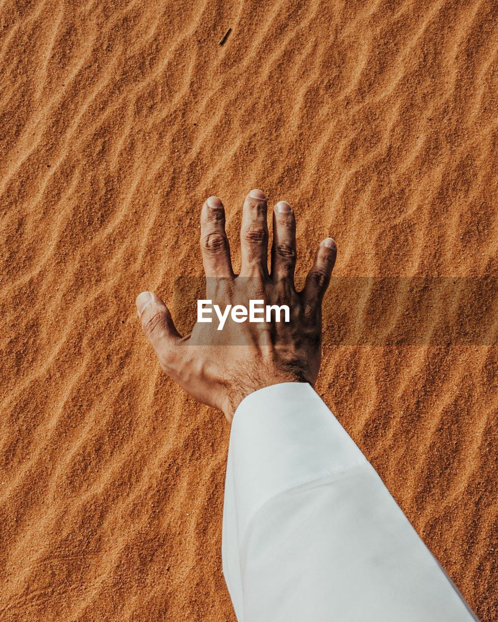 Cropped hand of man gesturing against sand in desert