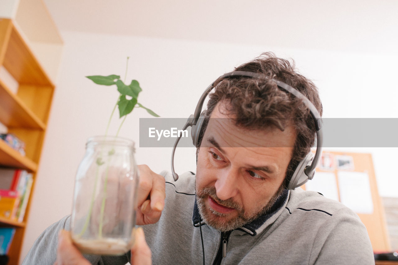 Mature adult male teacher explaining root growth of plant  in home schooling video conference,