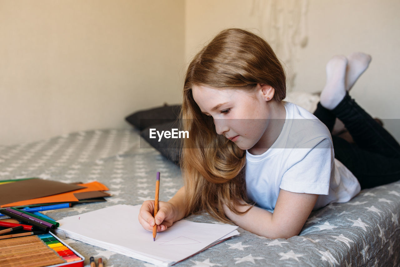 The girl after school plays at home, draws with pencils and felt-tip pens