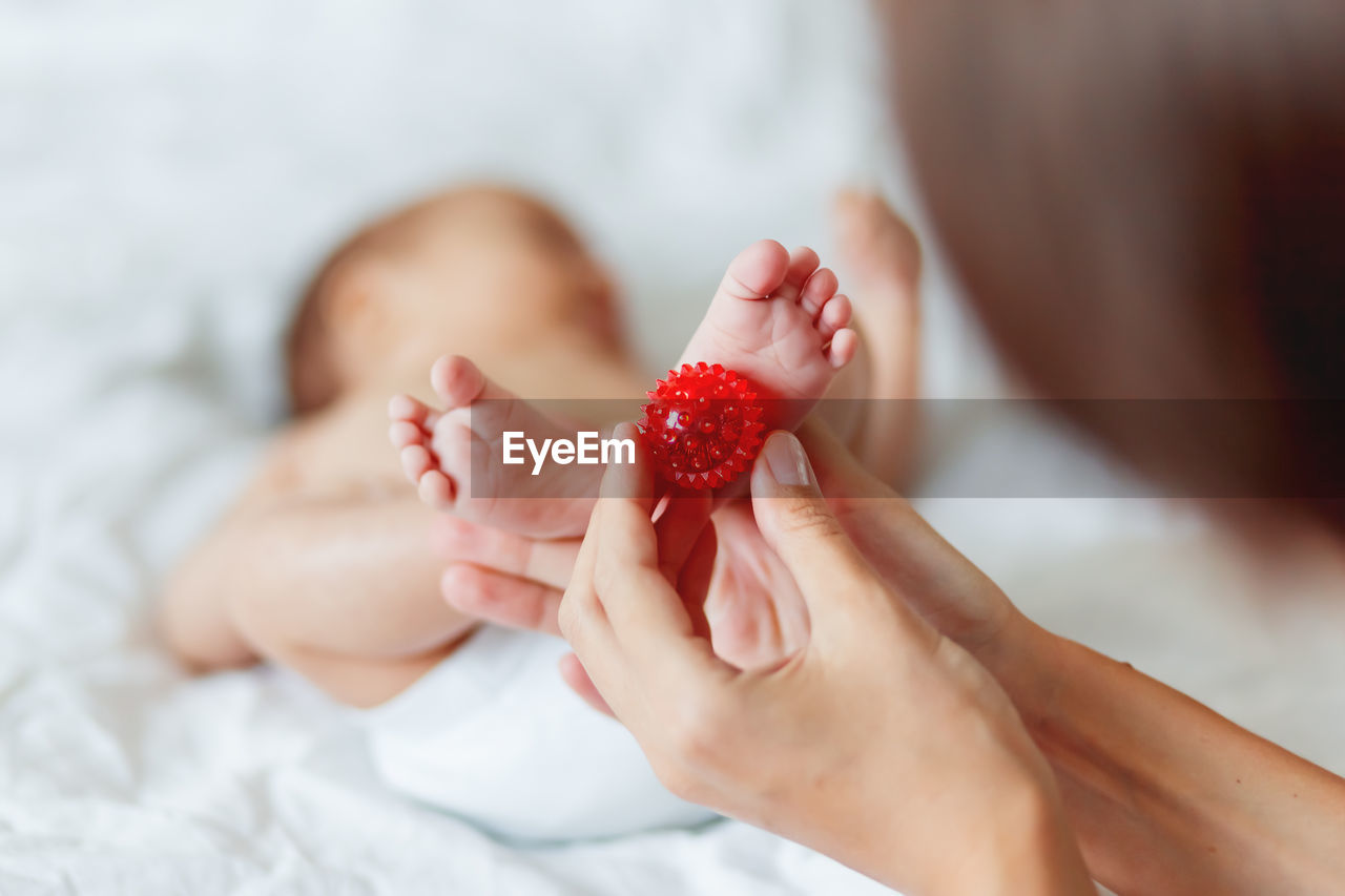 Mother holds newborn baby's feet. tiny fingers and red massage ball in woman's hand.
