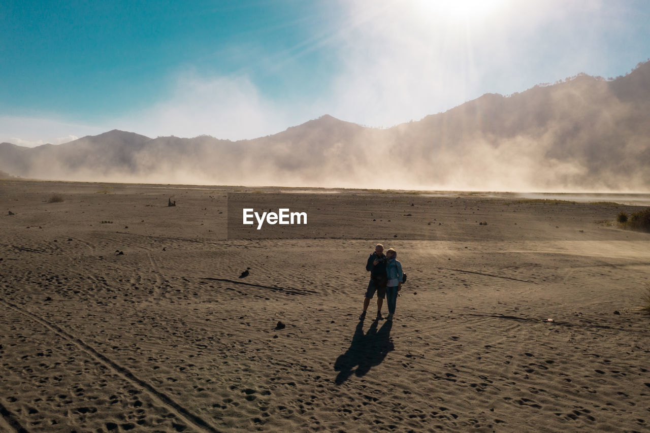 MAN WALKING ON DESERT AGAINST MOUNTAIN