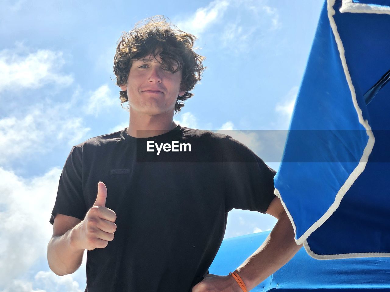Young man millennial give thumbs up at the beach in summertime.