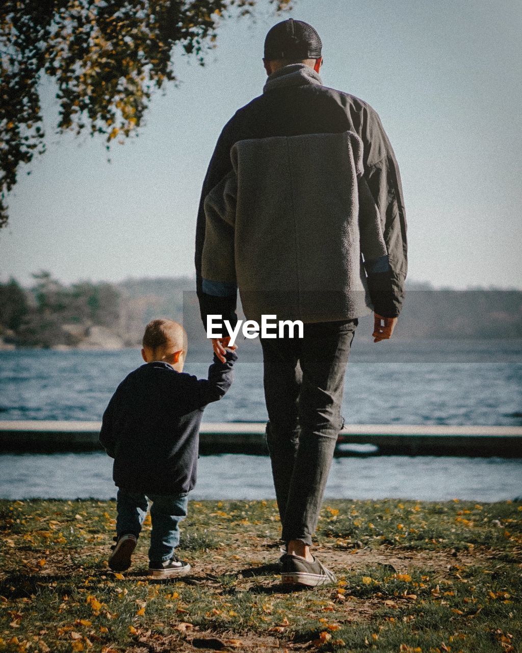 REAR VIEW OF MAN AND DAUGHTER STANDING ON SHORE