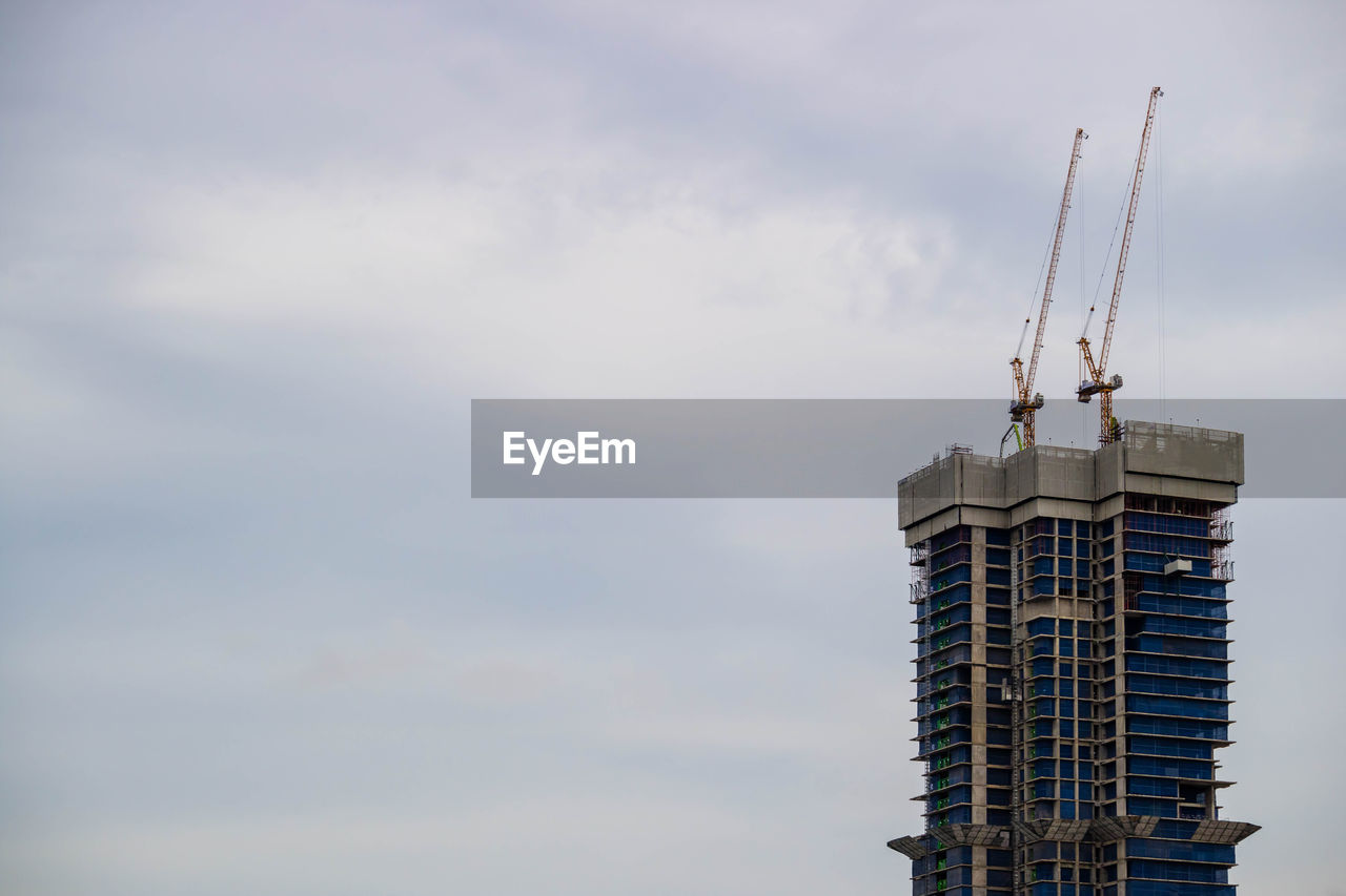 LOW ANGLE VIEW OF CRANE AGAINST CLOUDY SKY