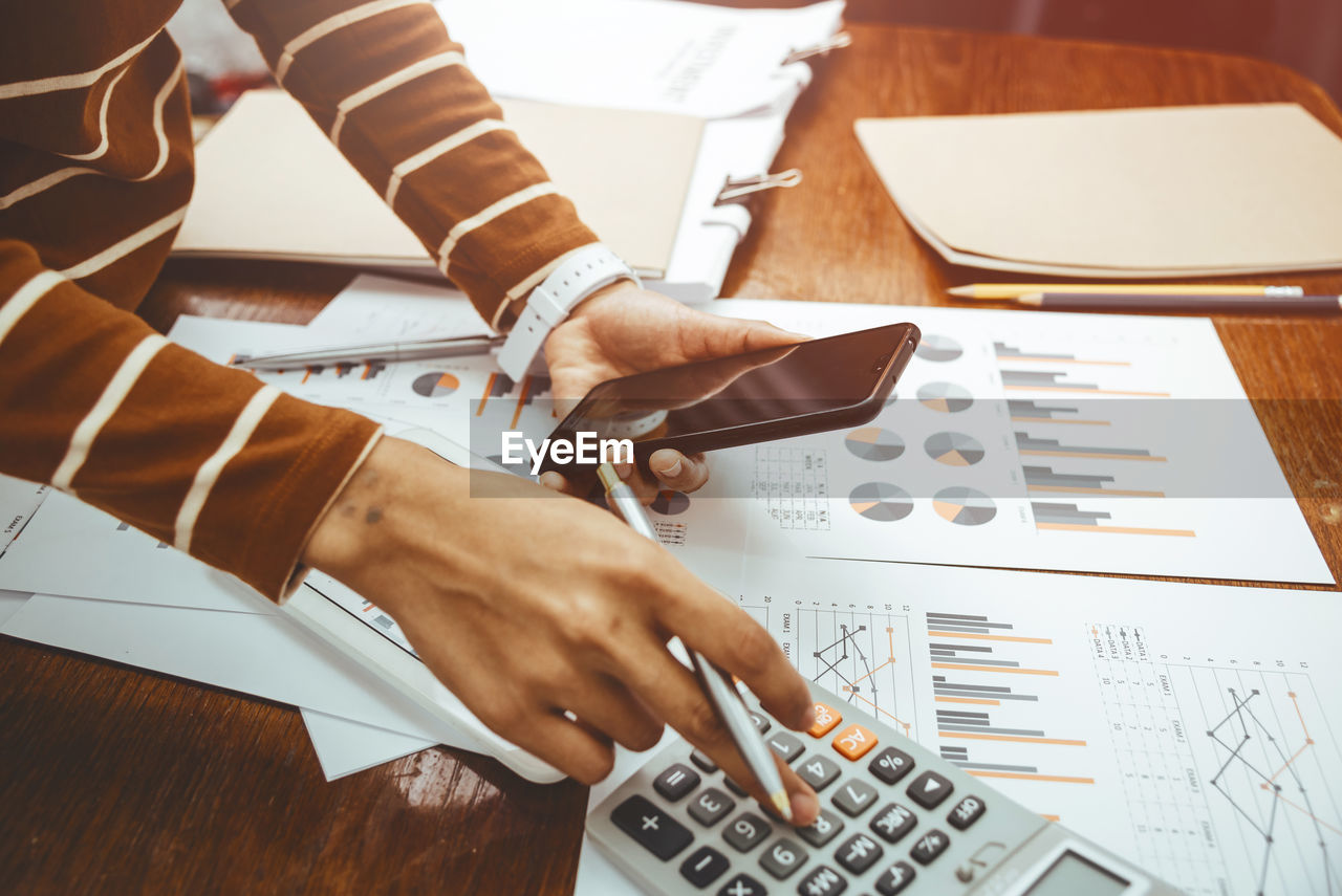 Midsection of businesswoman using smart phone and calculator in office