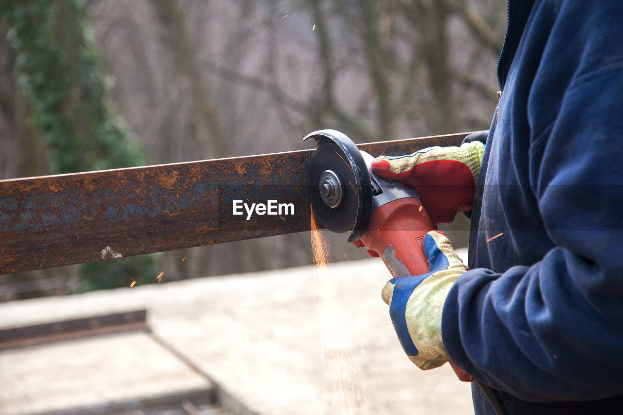 Midsection of man cutting metal with grinder