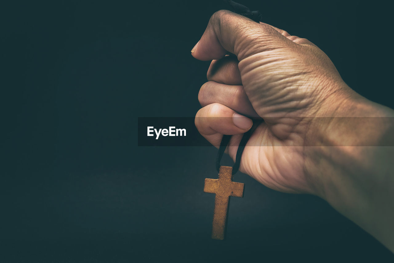 Close-up of hand holding cross against black background