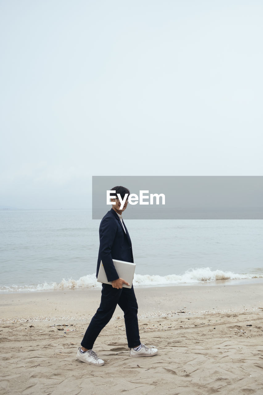 MAN STANDING ON BEACH AGAINST SKY