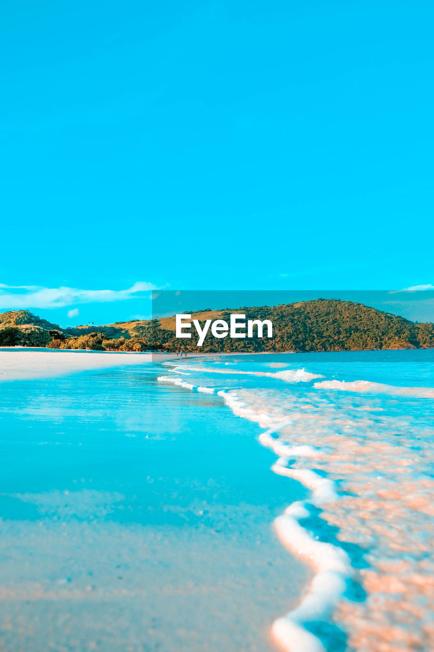 Surface level of swimming shore at beach against blue sky