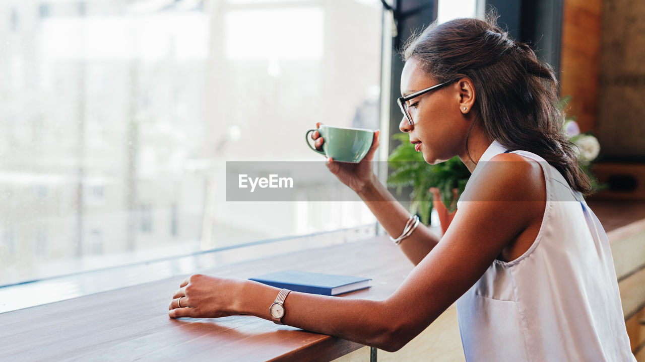 Woman drinking coffee while reading book at table