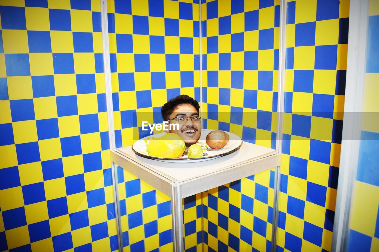 PORTRAIT OF A SMILING YOUNG MAN IN GLASS ON FLOOR