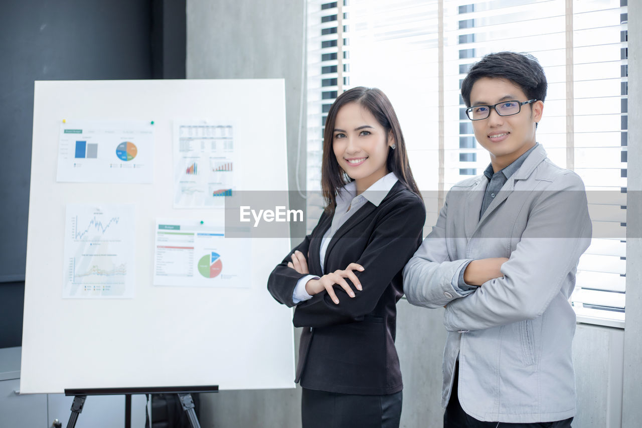 Portrait of smiling colleagues with arms crossed standing by whiteboard in office