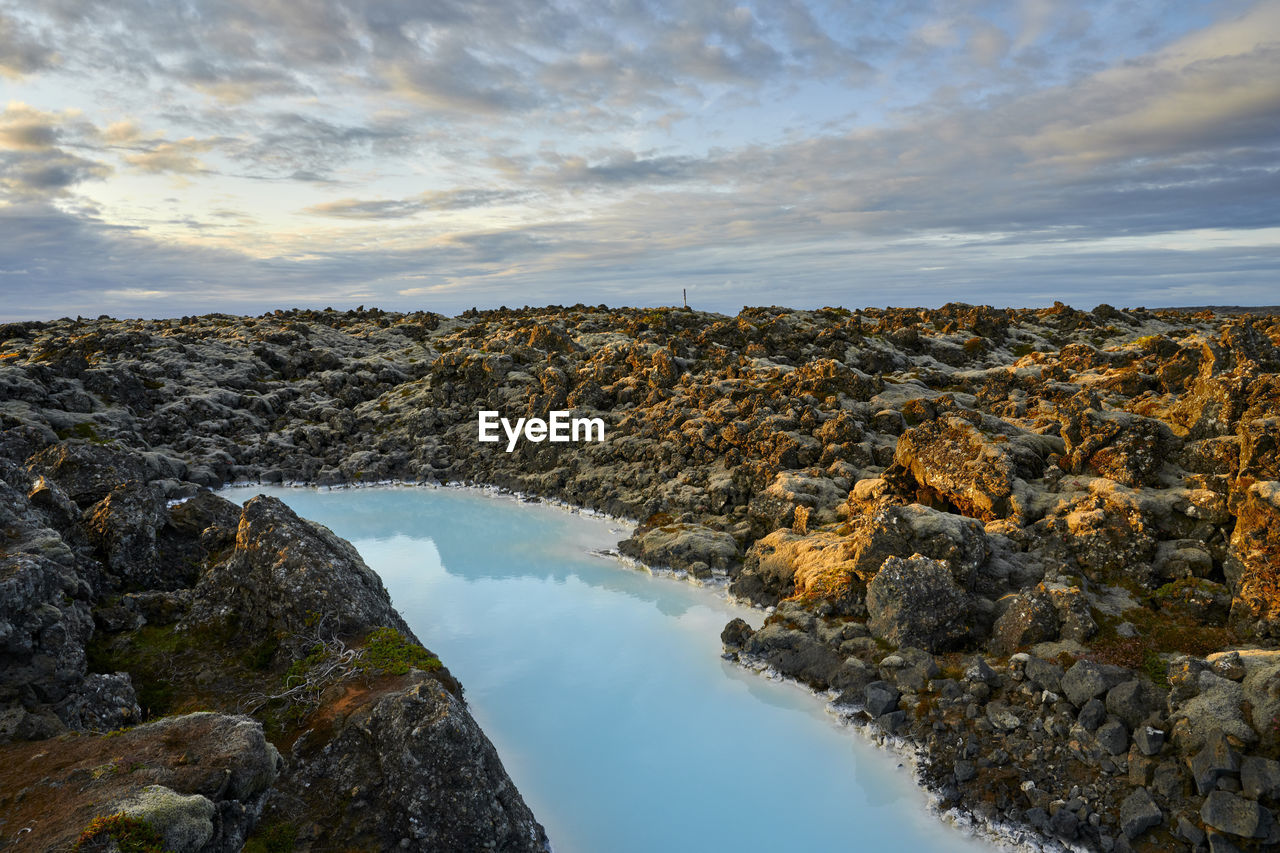 Picturesque landscape of geothermal spring in rocky terrain at sunset