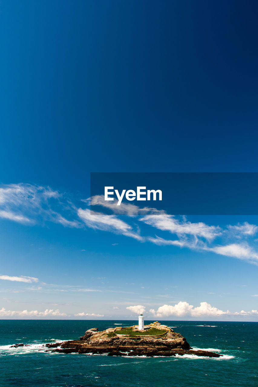 Lighthouse on rock formation in sea against sky