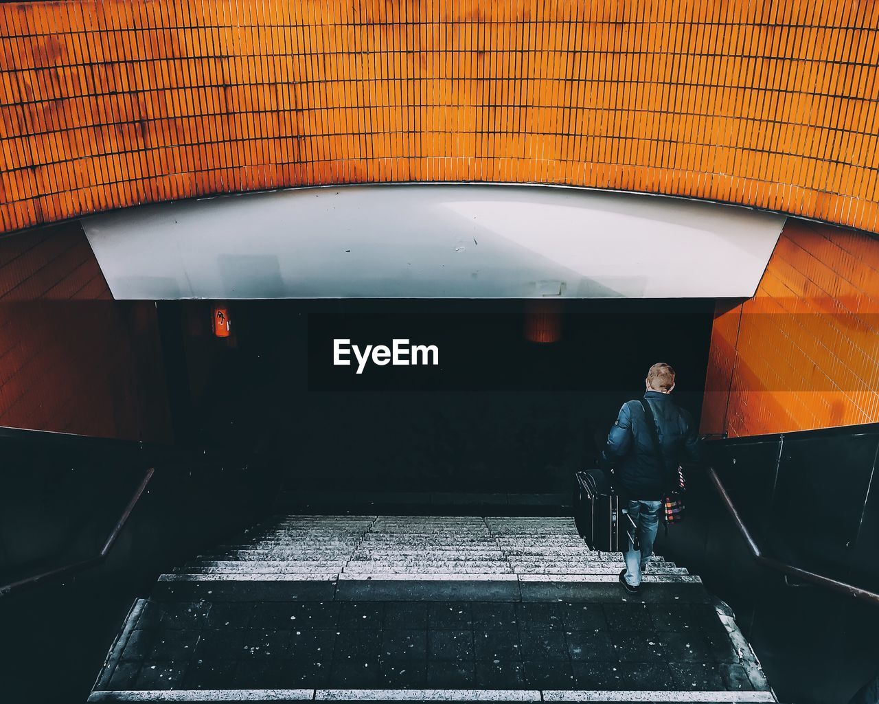 Rear view of man with luggage moving down steps at underground walkway