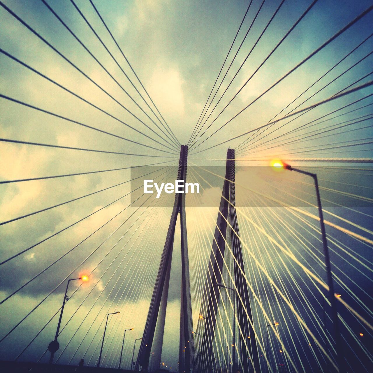 Low angle view of bridge and street light against cloudy sky