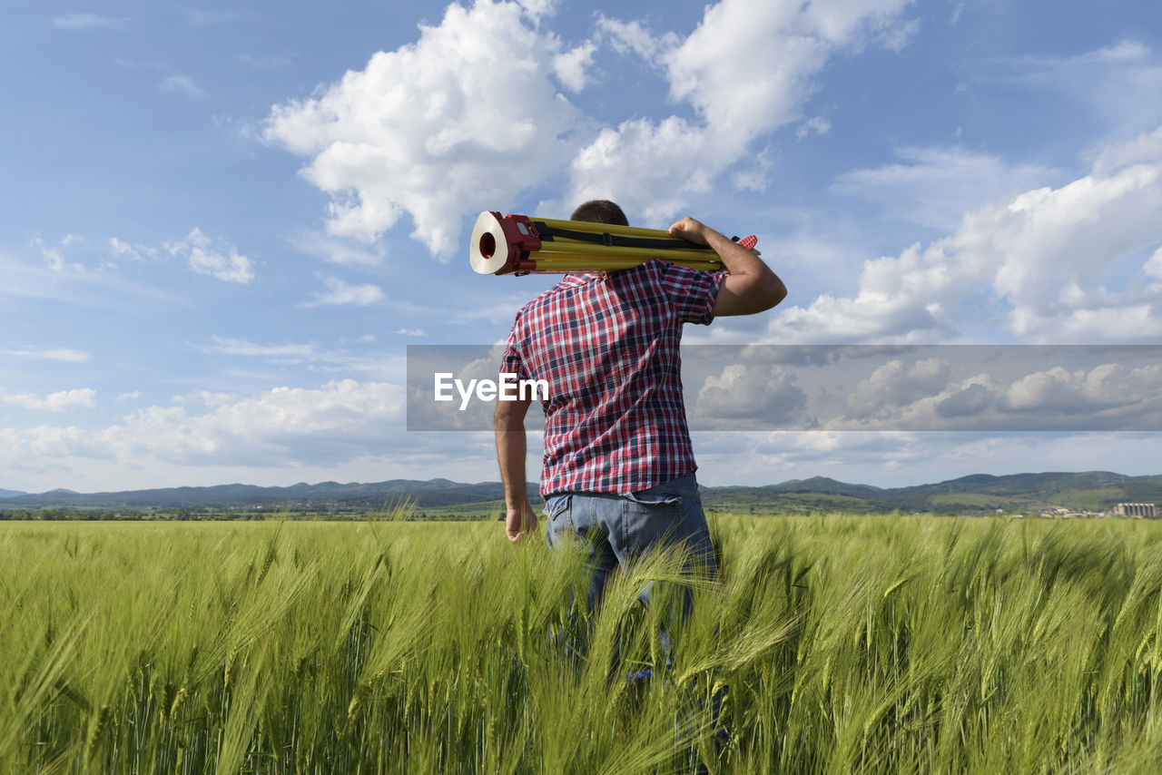 Rear view of engineer with equipment standing on wheat field