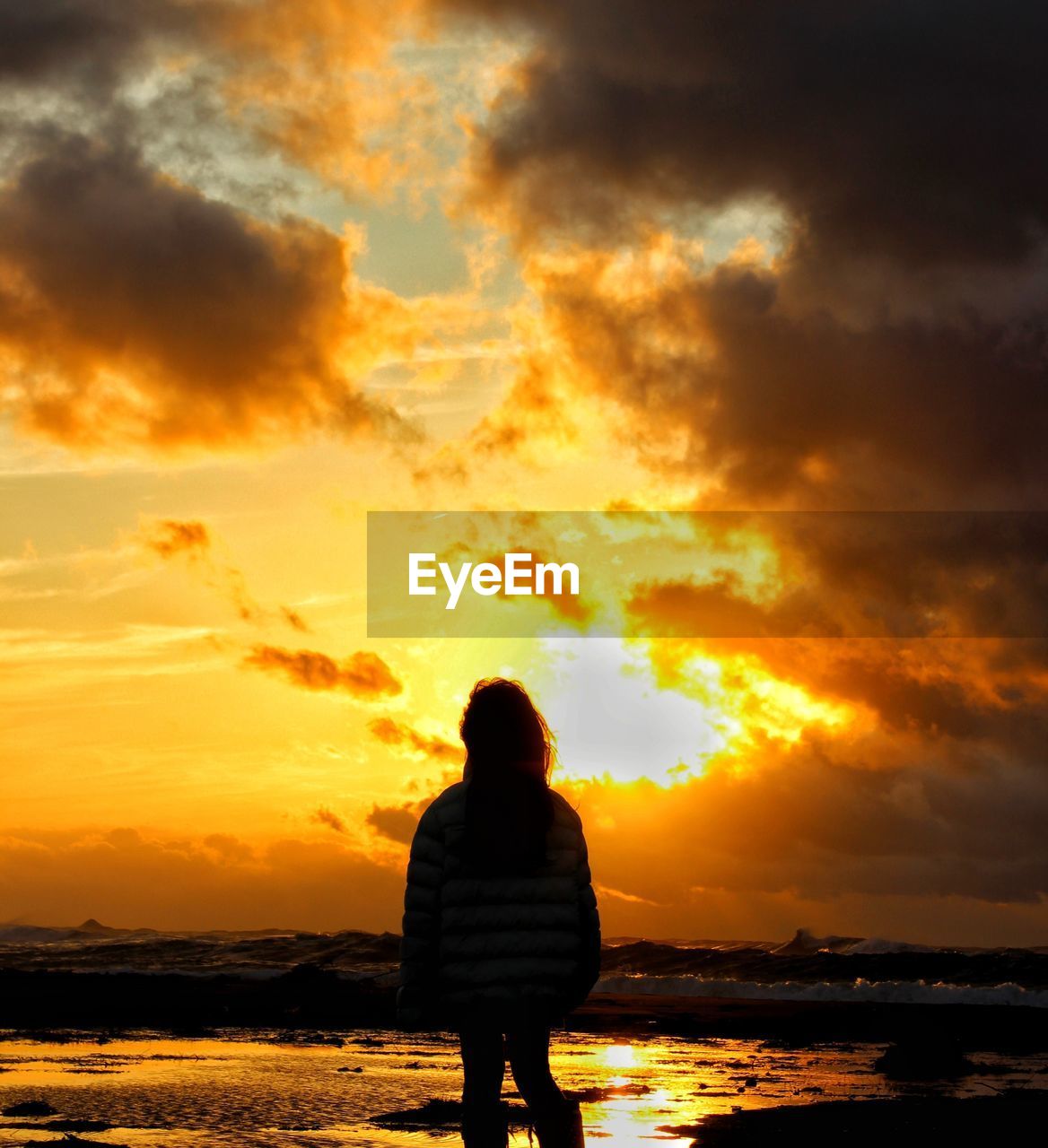 Rear view of silhouette woman standing against sky during sunset