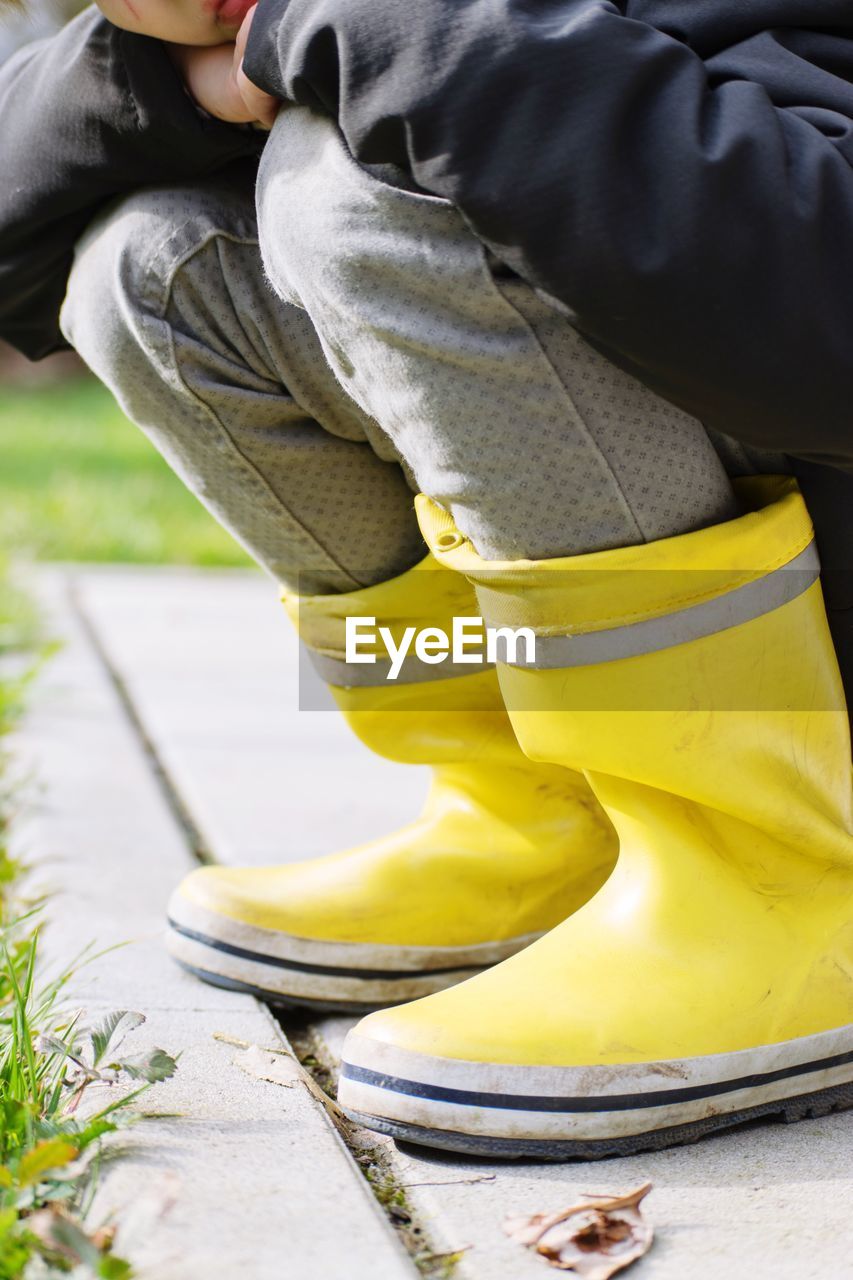 Low section of child wearing rubber boots on footpath