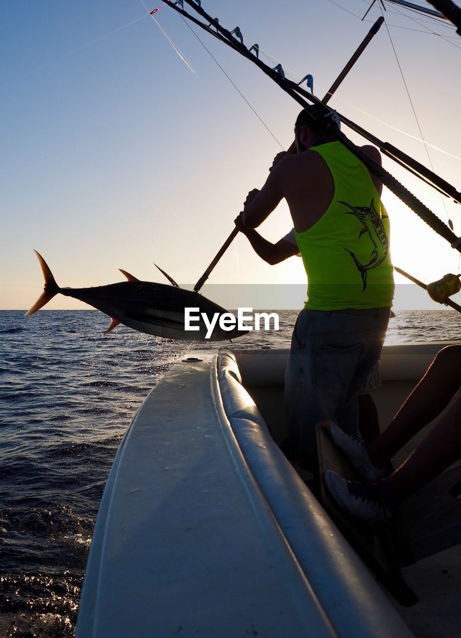 Rear view of man catching fish from boat on sea