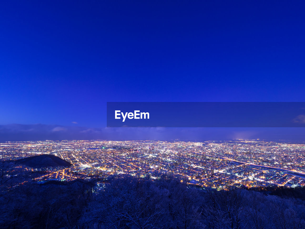 Aerial view of illuminated cityscape against blue sky