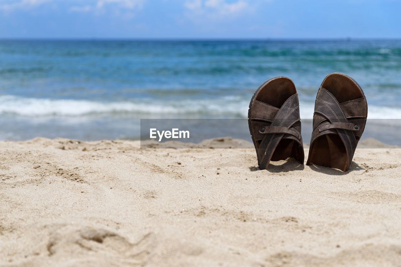 Shoes in the sand at beach against sky