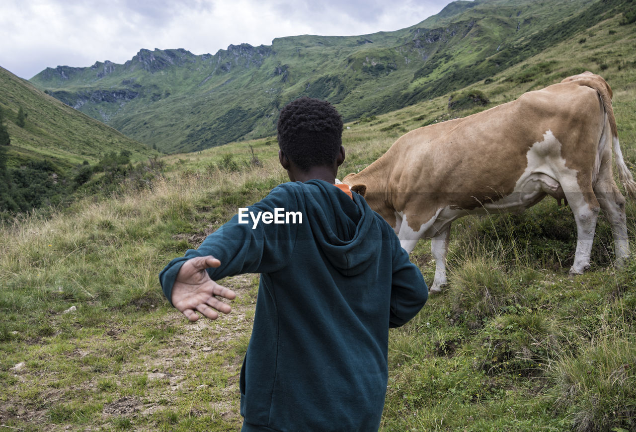 REAR VIEW OF MAN ON FIELD AGAINST MOUNTAIN