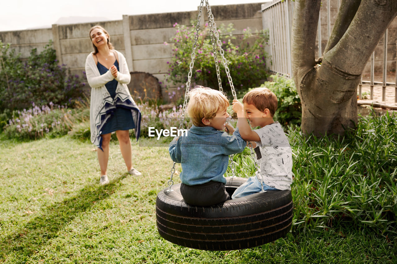 Smiling mother standing while kids playing on swing