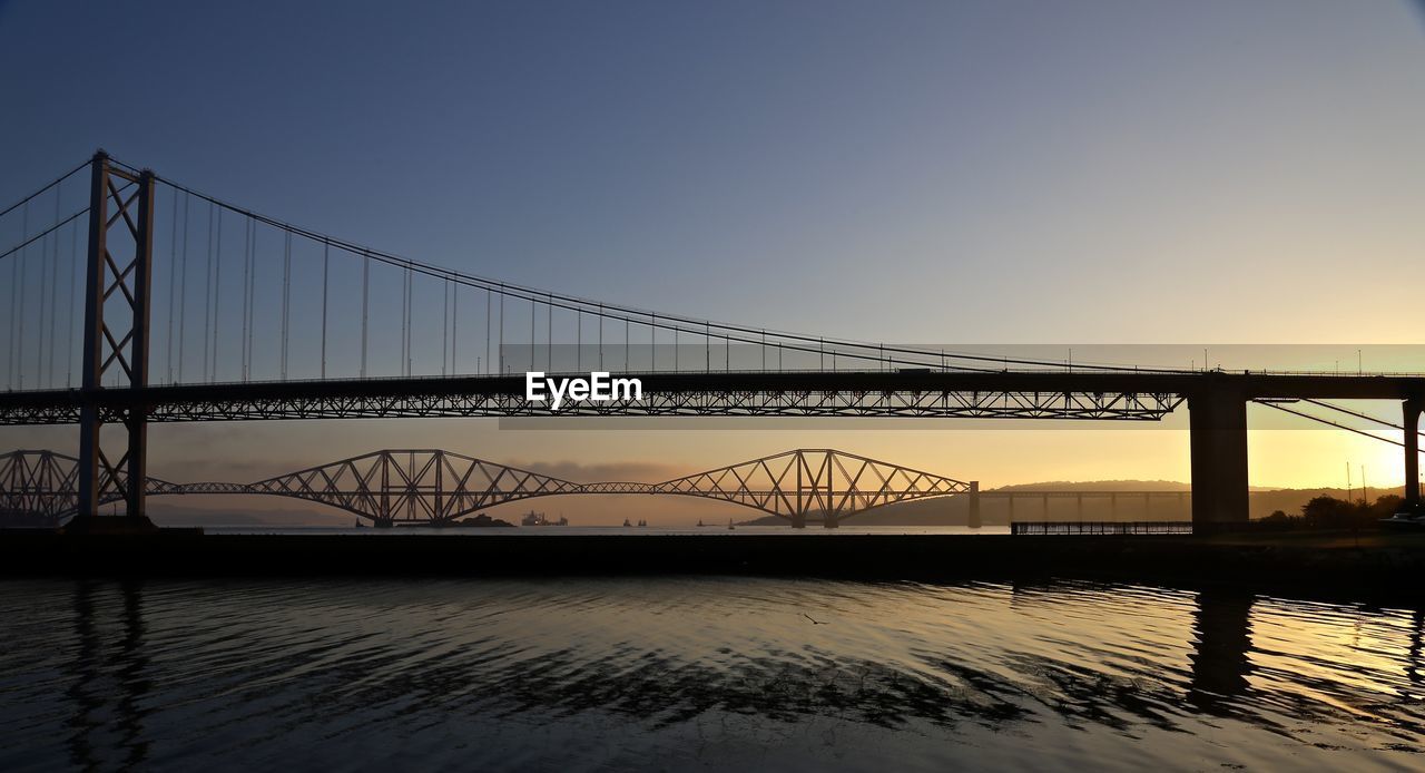 Forth road and rail bridge over river against clear sky at sunset