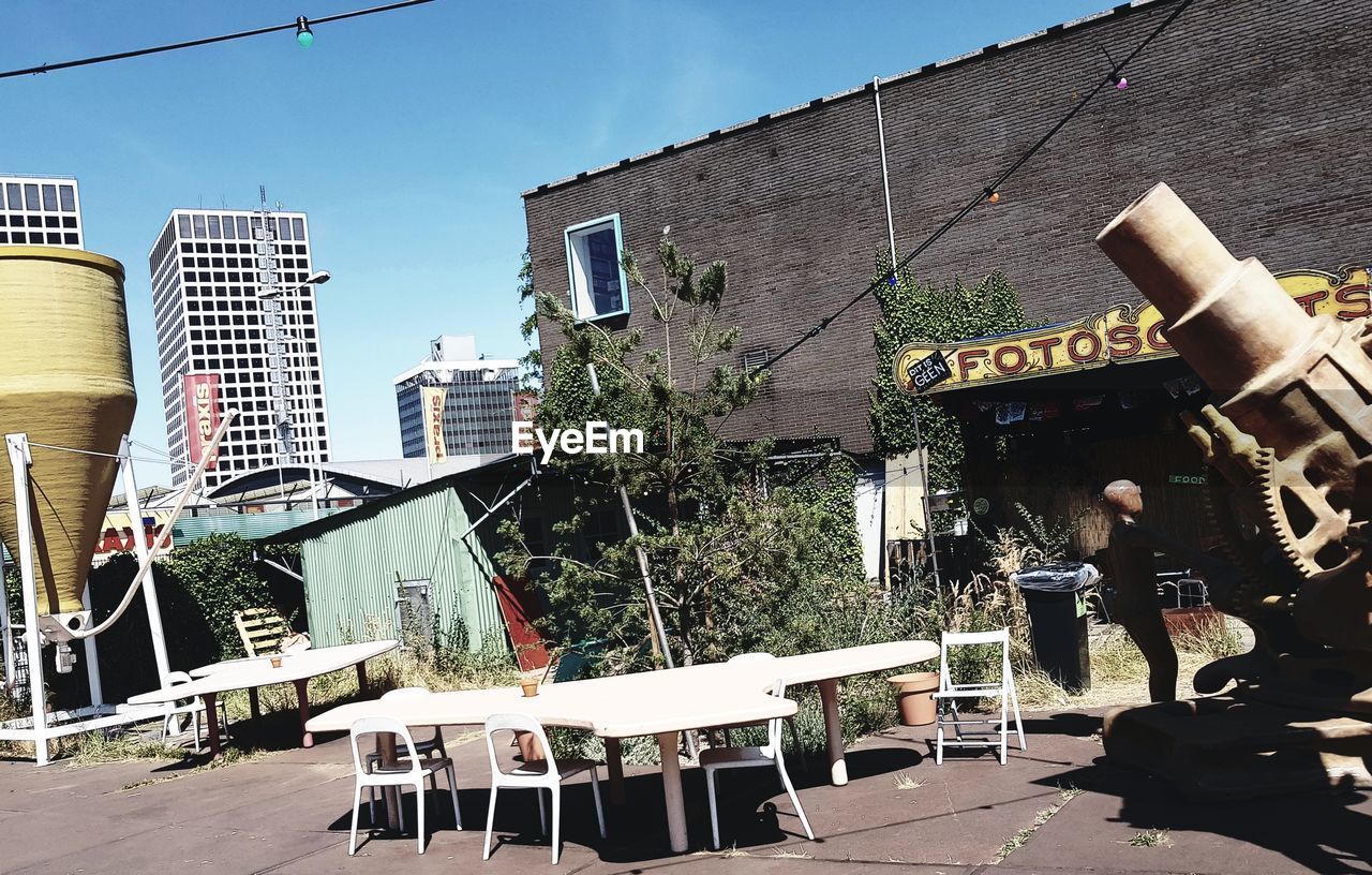 CHAIRS AND TABLE BY BUILDINGS AGAINST SKY