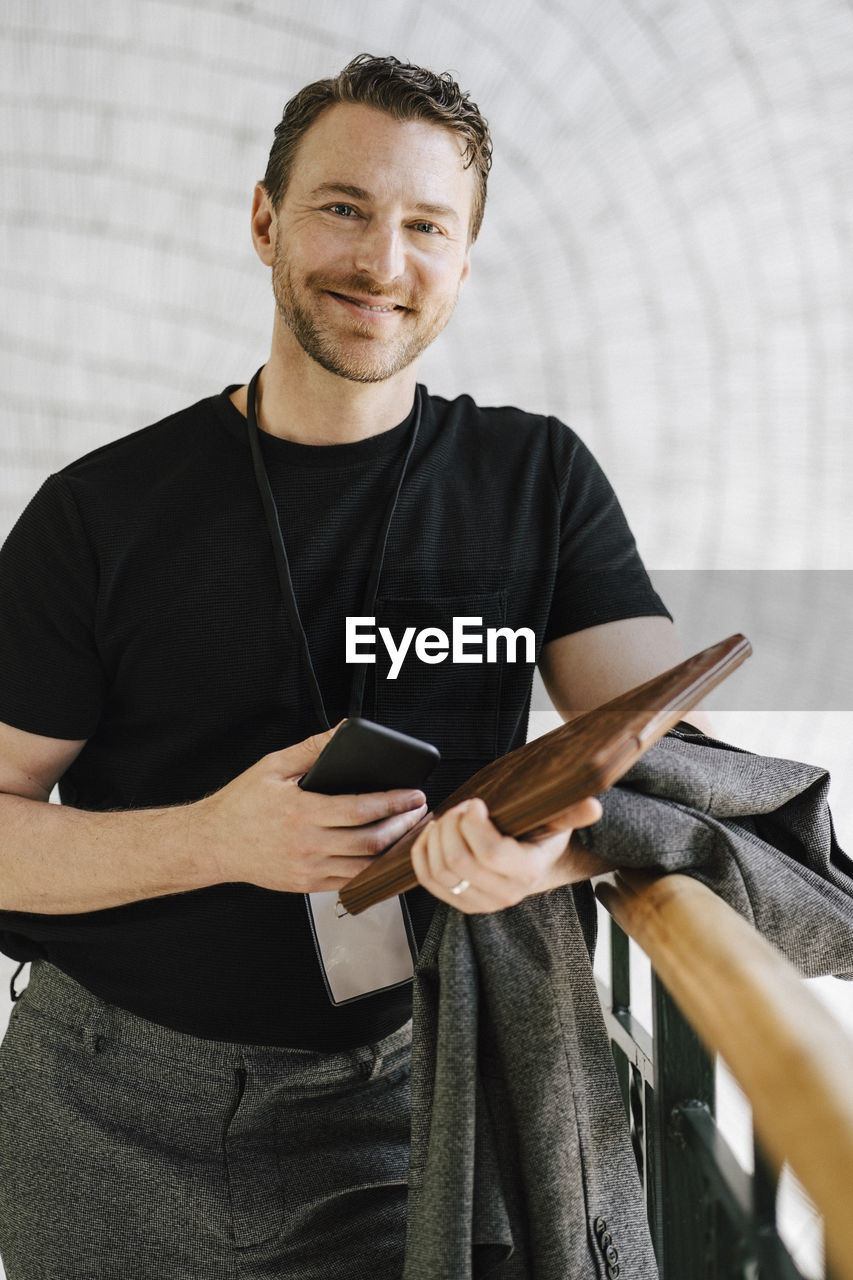 Portrait of smiling male professional standing with mobile phone and file at convention center