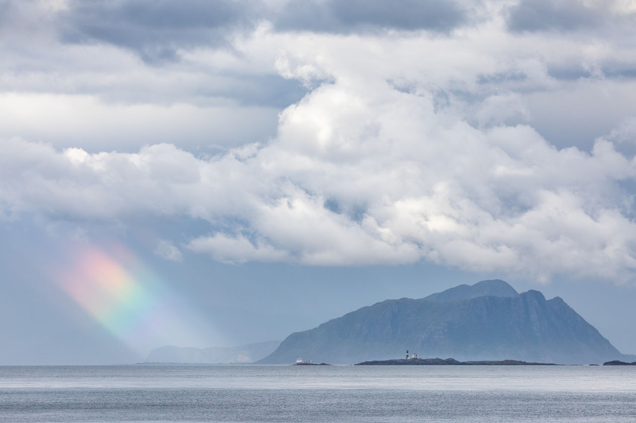 Rainbow spot lit by sunbeam against rocky islands in norwegian sea and moody sky