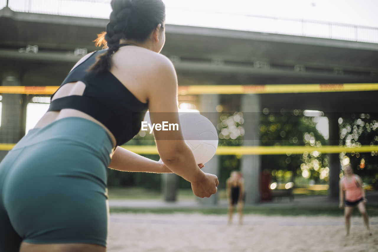 Woman serving volleyball while playing with friend