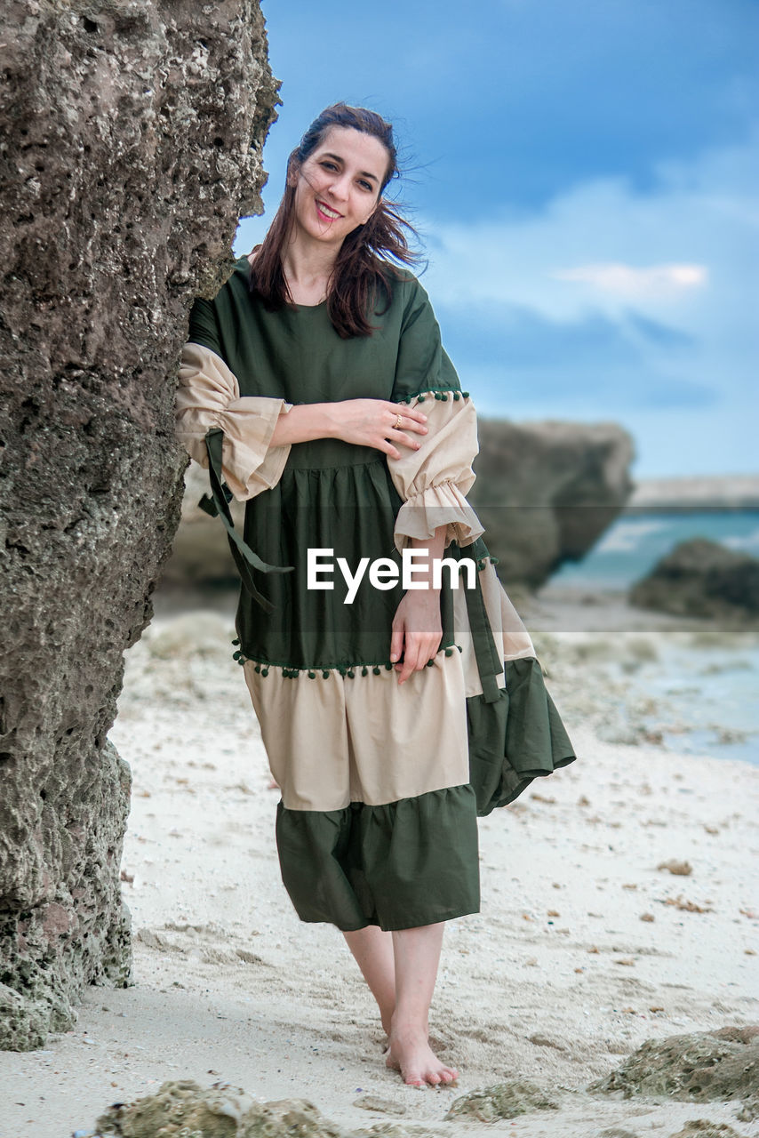 portrait of young woman standing on rock at beach against sky