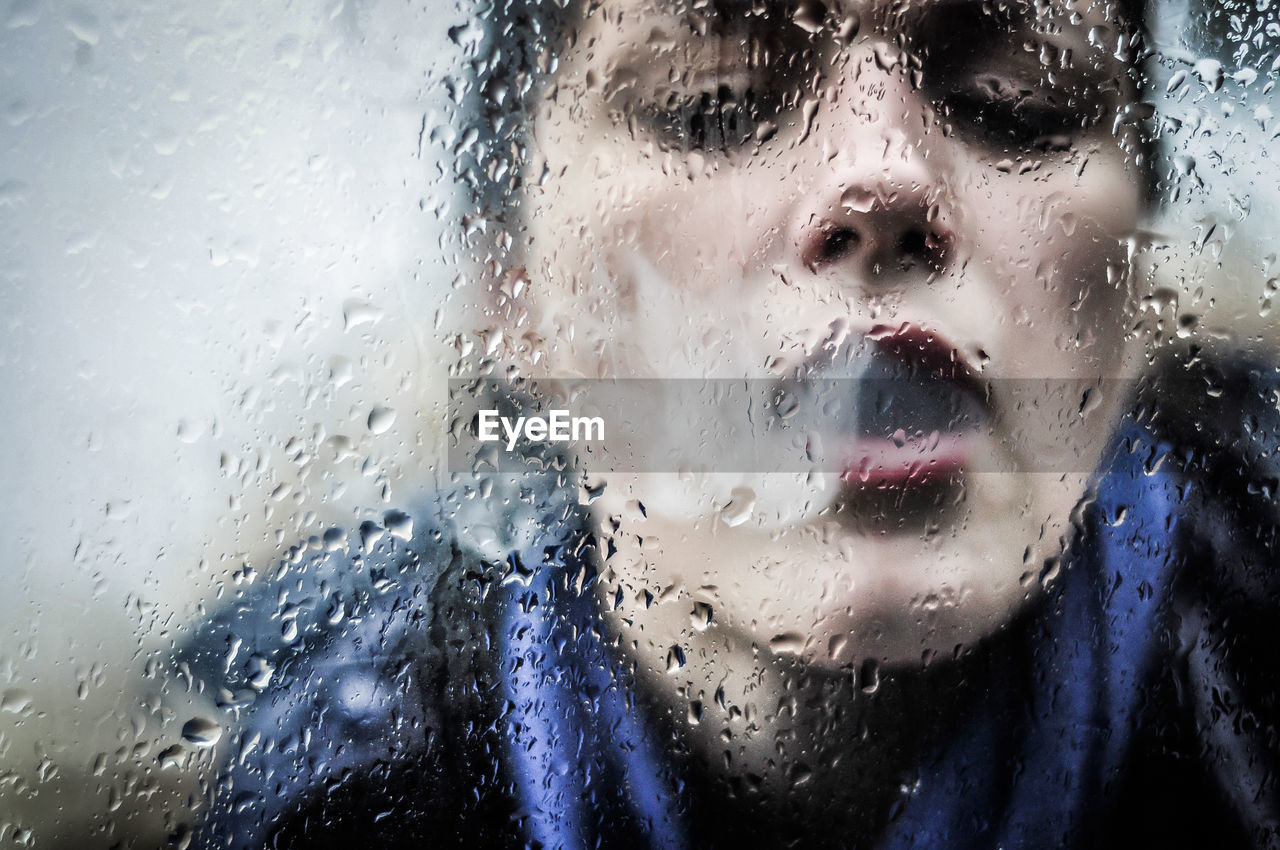 Close-up of woman emitting smoke on wet glass