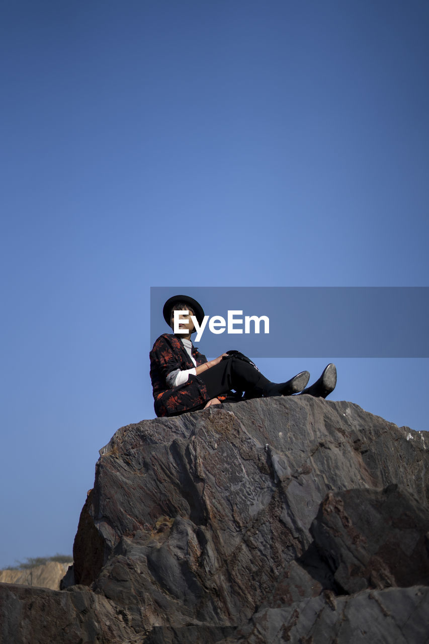 LOW ANGLE VIEW OF MAN SITTING ON ROCK