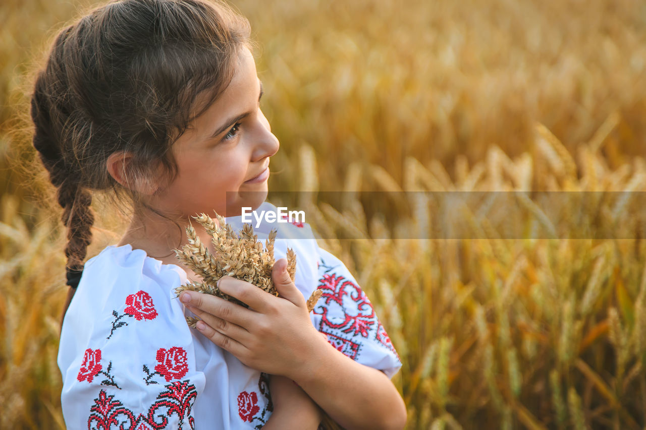 Cute girl holding wheat crops standing on field