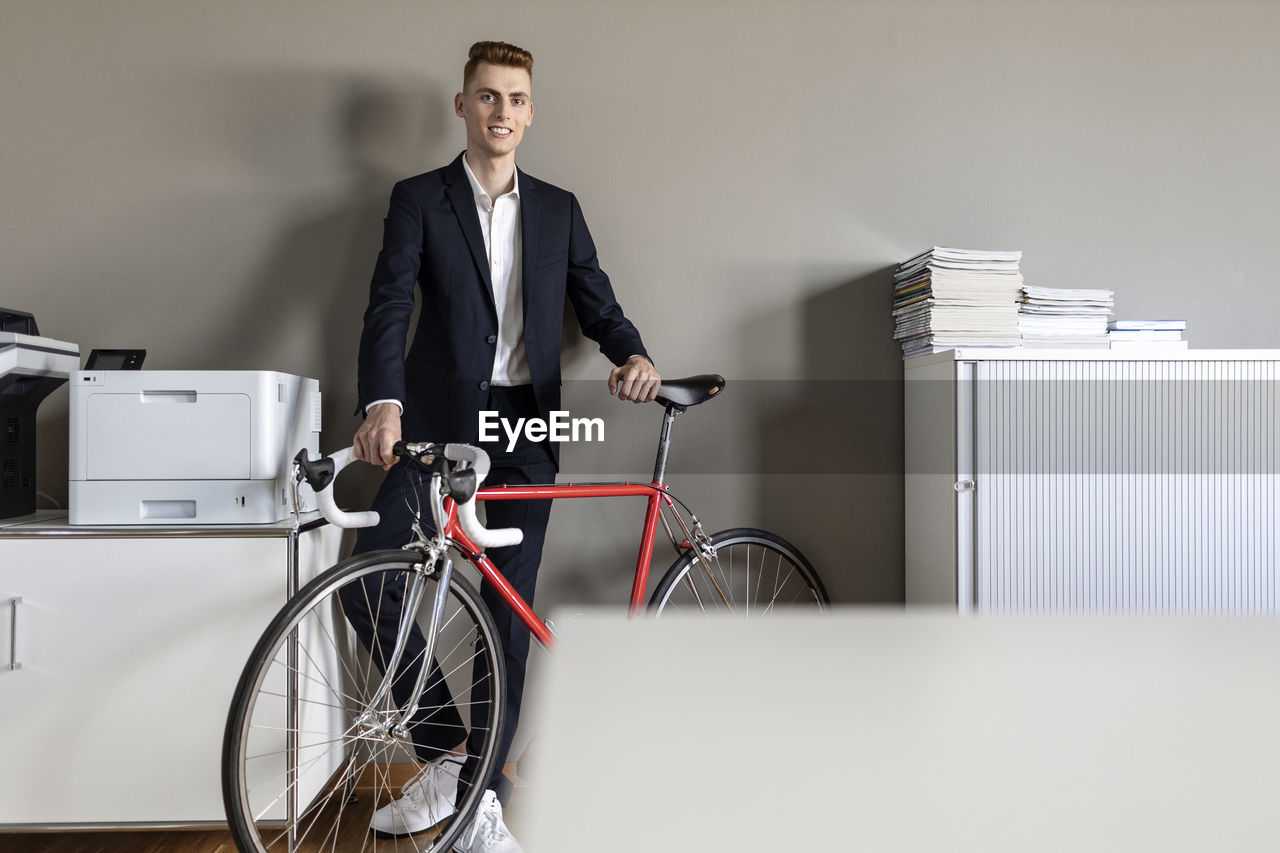 Businessman smiling while standing with bicycle at office