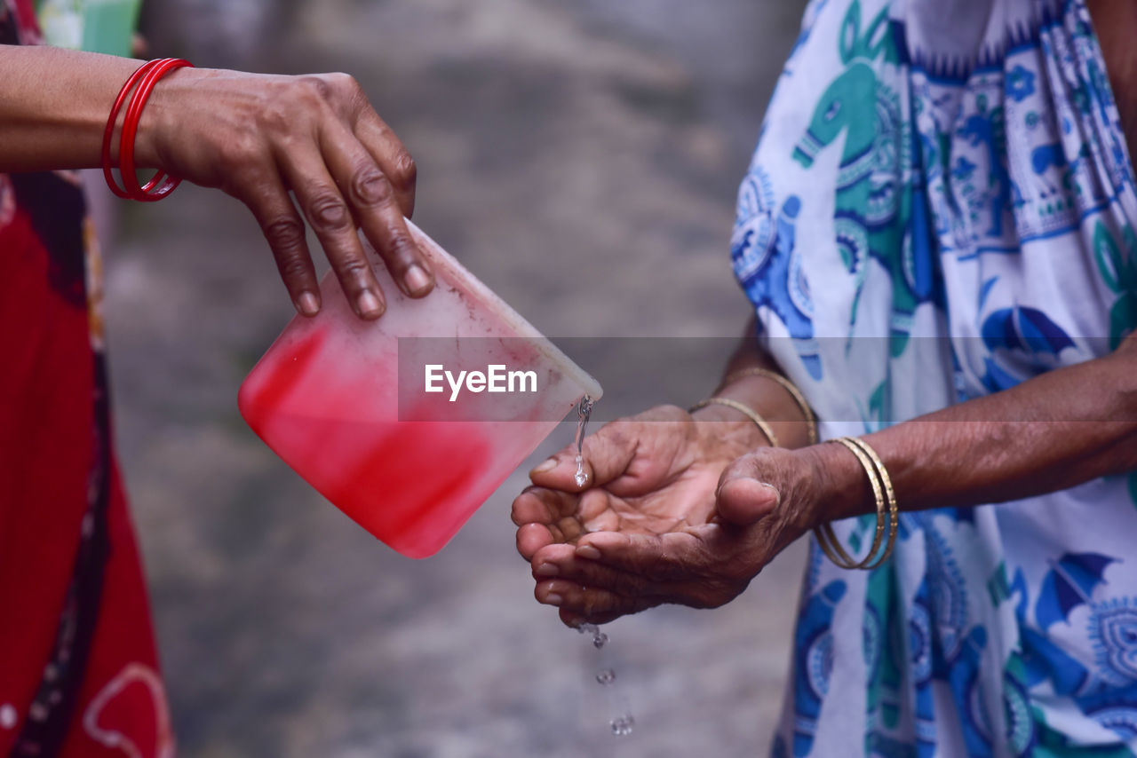 Cropped image of hand pouring water on woman hand
