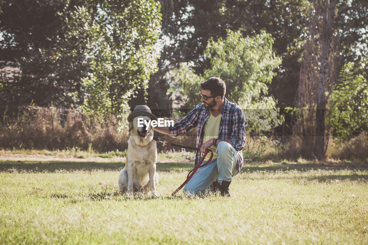 Mid adult man with dog wearing hat on grassy field