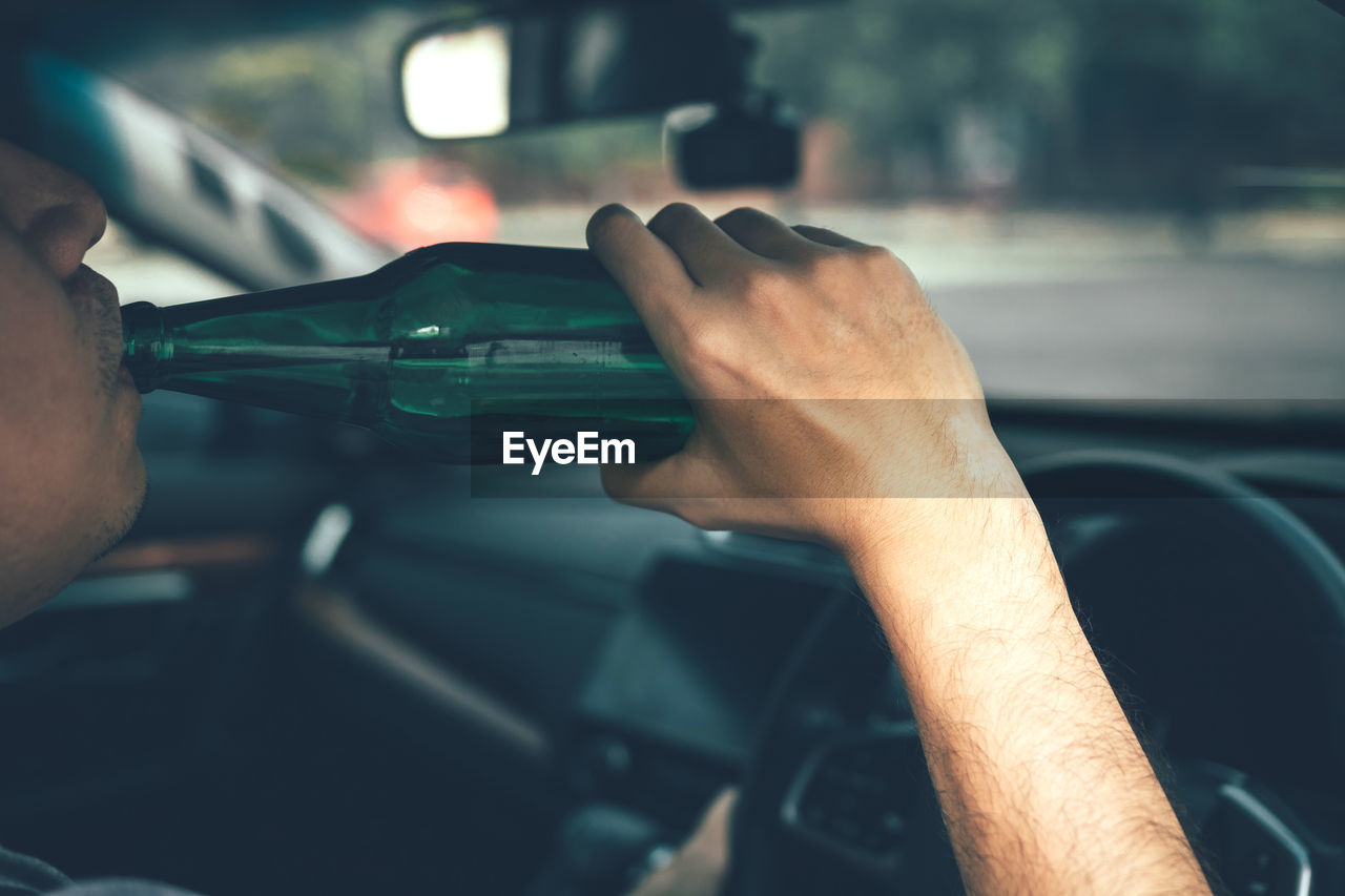 Cropped image of man drinking beer while driving car